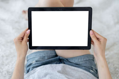 Virtual life. Digital mockup. Online entertainment. Unrecognizable relaxed woman looking tablet computer with blank screen laying bed in light room interior.の写真素材