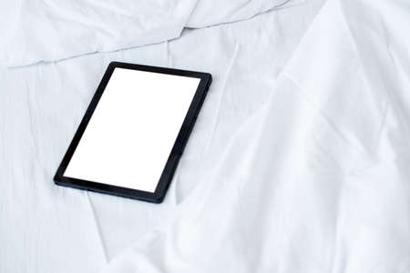 Digital life. Mobile mockup. Online connection. Tablet computer with blank screen laying bed in light room interior.の写真素材