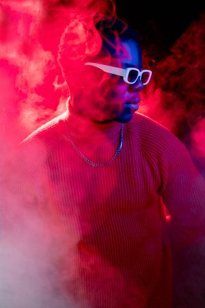 Neon hipster. Modern fashion. Nightclub party. Confident attractive man portrait in smoke flow vivid...