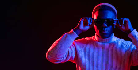 Neon light banner. Millennial nightlife. Eyewear fashion. Stylish attractive man in sunglasses in bright red glow isolated on dark copy space background.の写真素材
