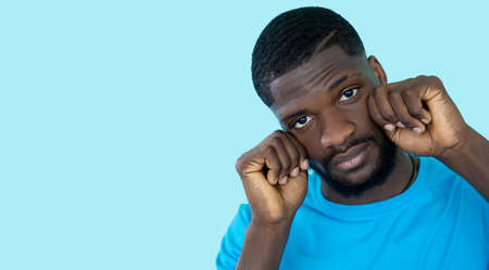 Crying man. Despair sorrow. Support community. Help banner. Unhappy frustrated guy wipes tears gesture isolated on blue empty space background.の写真素材