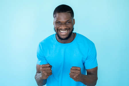 Celebrating man. Success joy. Goal achievement. Excited overjoyed happy young guy winner clenches fists on blue studio background.の写真素材