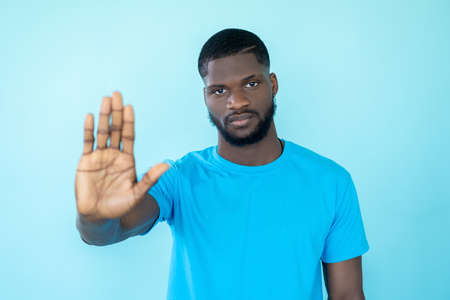 Stop gesture. Rejecting man. Warning sign. Racial tolerance. Serious strict guy showing outstretched hand refusal isolated on blue studio background.の写真素材