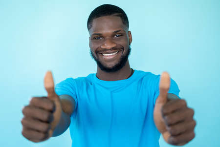 Approval gesture. Agree sign. Excellent idea. Support success. Joyful smiling satisfied man showing thumbs up isolated on blue background.の写真素材