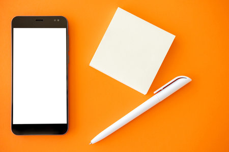 Digital mockup. Mobile technology. Make notes. Smartphone with white blank screen small papers and pen isolated orange flat lay.の写真素材