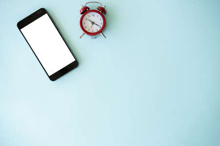 Online shopping. Mobile mockup. Sale time. Smartphone with white blank screen and alarm clock isolated blue background copy space.の写真素材