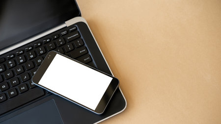 Digital mockup. Distance work. Online technology. Opened laptop and smartphone with white blank screen on beige table.の写真素材