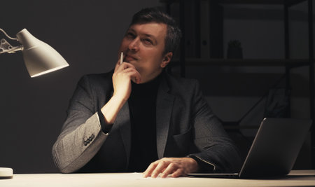 Vertical video. Inspiration muse. Pensive man. Late work. Creative thoughtful guy guessing ideas for writing sitting desk late dark room interior.の写真素材