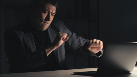 Vertical video. Successful project. Happy man. Online connection. Excited business guy having fun dancing sitting desk with laptop late dark room interior.の写真素材