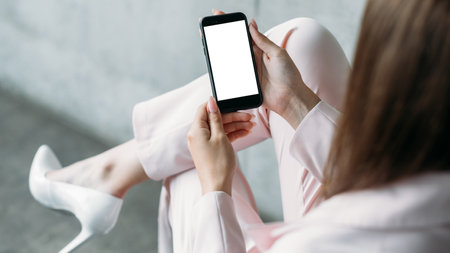 Online project. Digital mockup. Mobile technology. Elegant confident lady holding smartphone blank screen sitting chair in light room interior.の写真素材