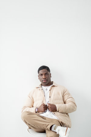 Fashionable lifestyle. Confident man portrait. Trendy guy in beige outfit sitting in studio
