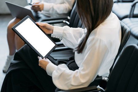 Office work. Computer mockup. Digital technology. Unrecognizable women holding tablet computer with blank screen sitting light room interior.の写真素材
