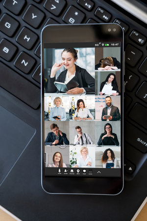 Virtual team. Video chat. Digital telecommuting. Professional business colleagues discussing work online on phone screen on laptop keyboard.の写真素材