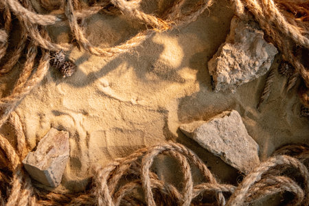 Nautical background. Sand frame. Marine layout. Rock pieces twisted rope pile composition sunlight on beige grain texture with free space.の写真素材