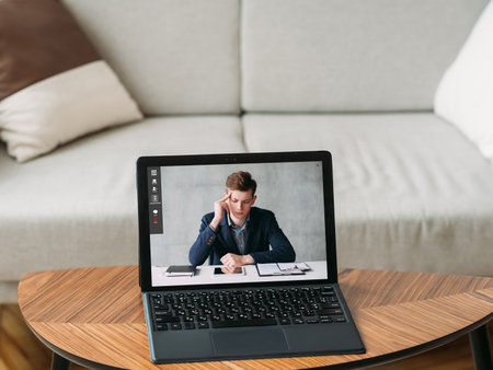 Video interview. Web chat. Online communication. Pensive business man on laptop screen at digital home office at couch with free space.の写真素材