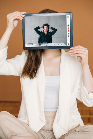 Female success. Video interview. Virtual presentation. Satisfied happy relaxed business woman smiling online on tablet screen in hands on brown.の写真素材