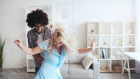 Morning fun. Home joy. Positive lifestyle. Inspired happy energetic diverse couple enjoying dancing spending life moments together in light room interior.の写真素材