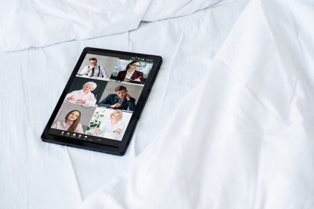 Home teleconference. Video chat. Digital meeting. Corporate business team working online on tablet screen on white bed sheets with free space.の写真素材