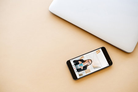 E-learning course. Video chat. Digital education. Flat lay of online female teacher on phone screen on pastel orange copy space background.の写真素材