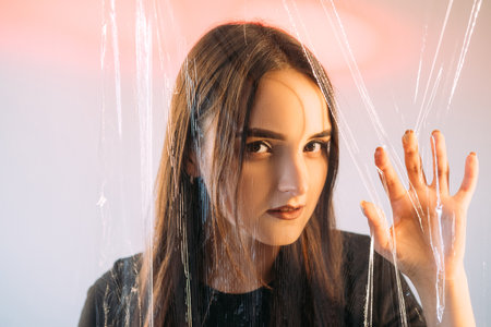Psychic medium. Fortune teller. Clairvoyant prophecy. Esoteric sorcerer. Portrait of mysterious woman face hand touching transparent polyethylene plastic film wall.の写真素材