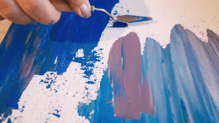 Abstract picture. Painting process. Art studio. Unrecognizable woman drawing on board canvas with spatula and colorful paints.の写真素材