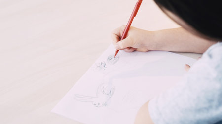 Painting hobby. Home relax. Creative kids art. Unrecognizable child drawing on white paper with pencil sitting table blurred.の写真素材