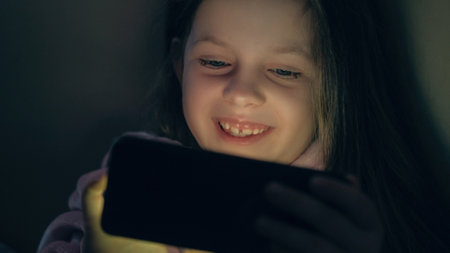 Child night movie. Gadget kid. Late fun. Entertained happy smiling little girl enjoying watching...