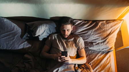 Phone night. Online insomnia. Late virtual communication. Bored sleepy depressed man surfing Internet using electronic gadget in bed in dark home bedroom.の写真素材