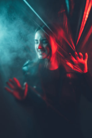 Emotional crisis. Mental disorder. Red blue color light defocused angry desperate mad woman silhouette trapped behind transparent plastic film wall in smoke on dark.の写真素材