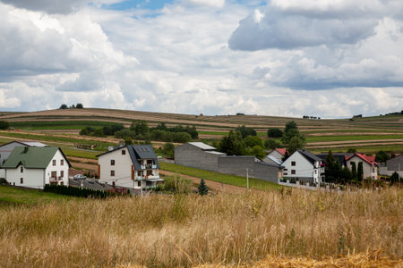 Countryside village. Rural scenery. Nature landscape. White cottage houses on meadow hills with harvest fields fluffy sky clouds daylight panorama.の写真素材