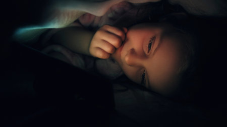 Kid bed movie. Night gadget. Bedtime entertainment. Curious impressed small girl enjoying watching...