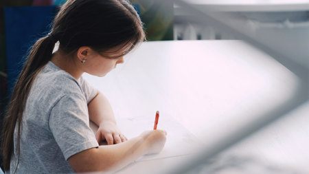 Art studio. Little girl. Painting lesson. Inspired kid drawing with pencil on white paper in light...