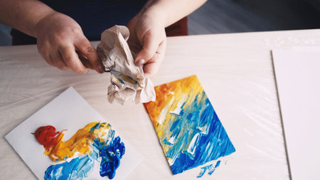 Finish artwork. Female painter. Artistic tools. Unrecognizable woman cleaning spatula after painting abstract picture on canvas.の写真素材