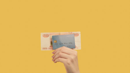 Money loan. Bank transaction. Woman hand holding rubles 5000 and credit card on yellow background.の写真素材