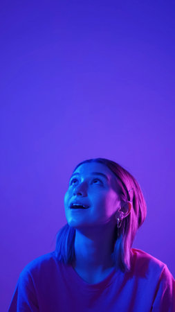 Impressed girl portrait. Amazed promotion. Neon color light startled woman looking up saying wow isolated on blue pink empty space background.の写真素材
