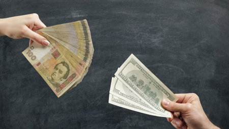 Money trade. Currency exchange. Woman hand giving hryvnia banknotes for man with dollars on chalkboard background.の写真素材