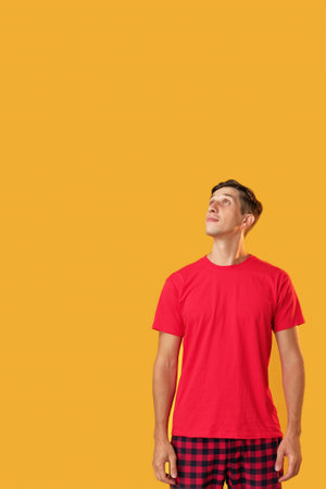 Surprised man portrait. Amazing advertising. Astonished guy in red looking up with excited face isolated on yellow copy space background.の写真素材