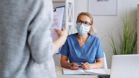 Medical consultation. Doctor office. Body check. Female in protective mask examining patient in...