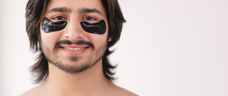 Facial patches. Male beauty care. Cheerful smiling man with under eye hydrogel black pads on face isolated on white empty space background.の写真素材