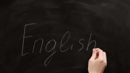 English school. Foreign language study. Female teacher hand writing word on black chalkboard.の写真素材