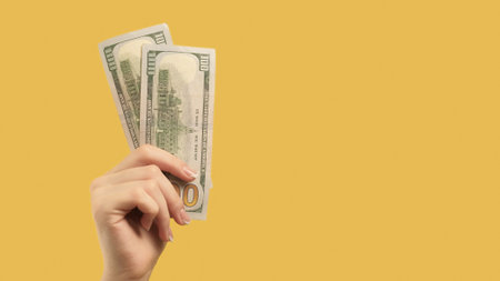 Money gesture. Profitable investment. Woman hand with doubled 100 dollar note on yellow background copy space.の写真素材