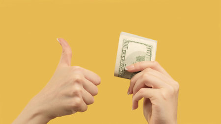 Passive income. Agreed gesture. Woman hands showing dollars and like sign d on orange yellow background.の写真素材
