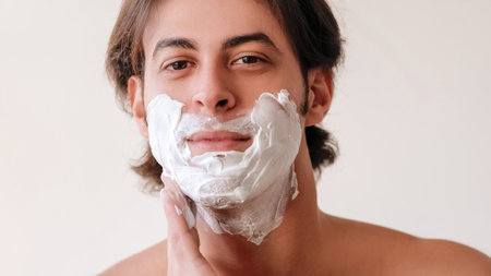 Morning shaving. Skin treatment. Grooming routine. Attractive undressed guy applying face foam isolated on white empty space background.の写真素材