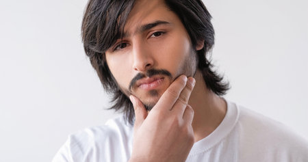 Beard care. Facial grooming. Pensive face. Unshaven guy with stubble mustache touching smoothing bristle isolated on white copy space background.の写真素材