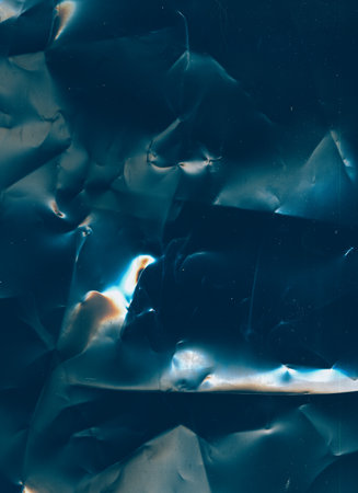 Creased overlay. Dust scratches noise. Old film texture. Blue orange black color glow on dark wrinkled uneven foil surface illustration abstract background.の写真素材