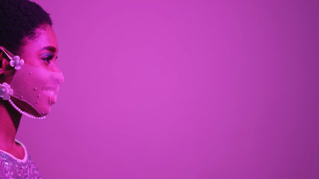 Quarantine fashion. Face accessory. Pandemic party. Purple pink color neon light profile portrait of confident smiling woman in mesh mask on fluorescent empty space background.の写真素材