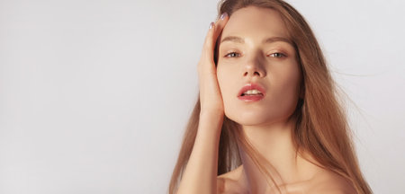 Moisturizing skincare. Facial treatment. Skin freshness. Woman with nude makeup hand touching flawless radiant face isolated on grey background empty space.の写真素材