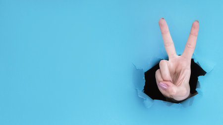 Peace gesture. Victory sign. Female hand showing number two with fingers inside breakthrough paper...