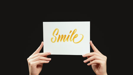 Smile sign. Positive motivation. Cheering slogan. Female hands encouraging with optimistic message text placard isolated on dark black empty space background.の写真素材