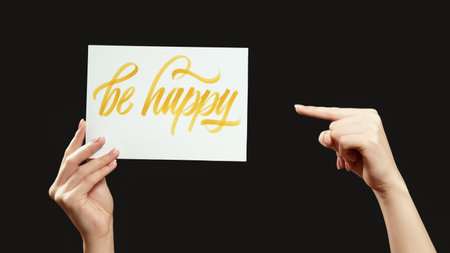 Be happy. Positive motivation. Female hand showing pointing finger at encouraging support slogan isolated on black free space background.の写真素材